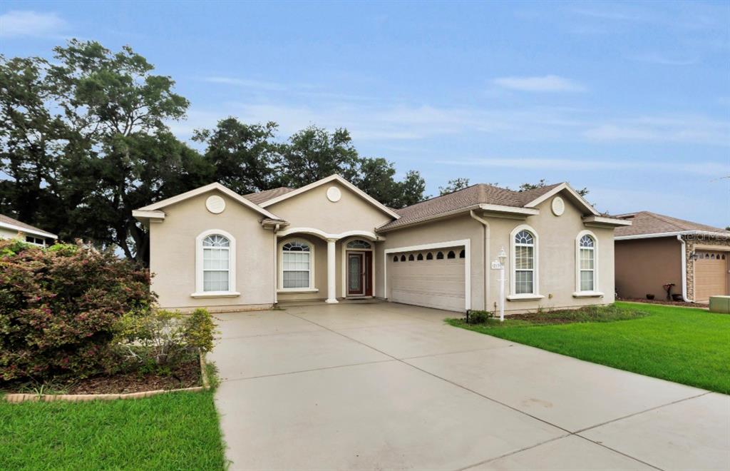 A single-story suburban house with a beige stucco exterior, arched windows, and a concrete driveway — 12139 SE 175TH LOOP, SUMMERFIELD, FL