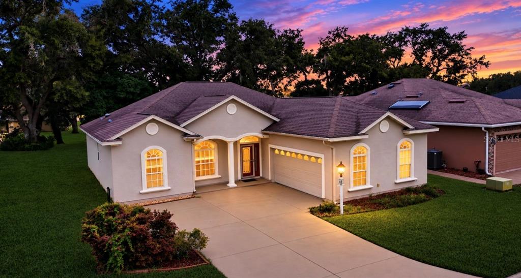 An exterior view of a single-story beige house with a driveway and a sunset sky — 12139 SE 175TH LOOP, SUMMERFIELD, FL