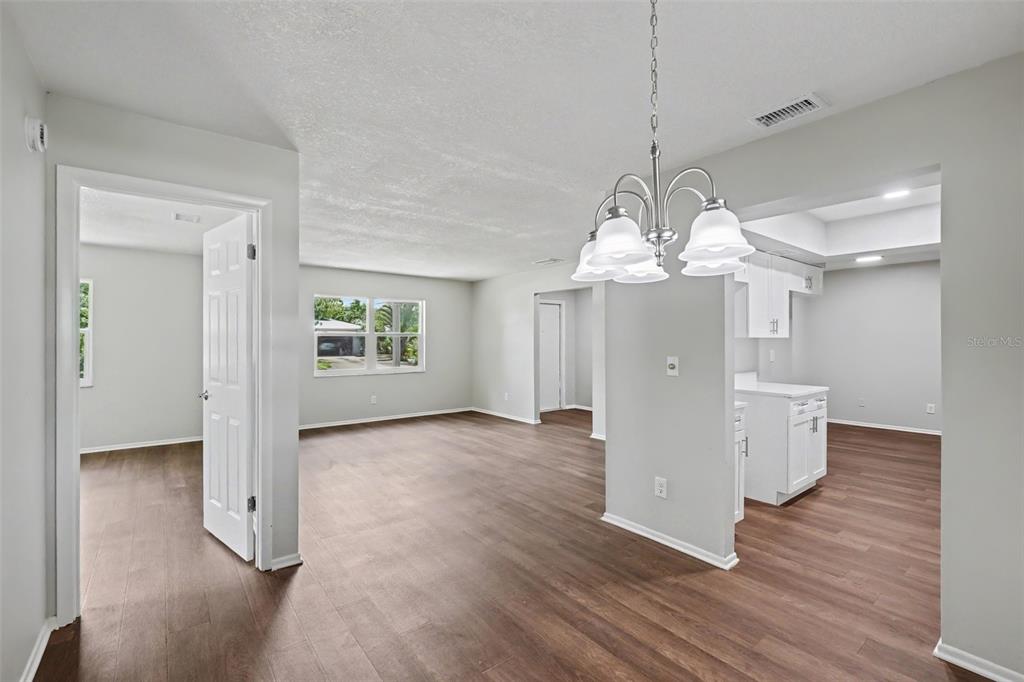 An open-concept living and dining area with light gray walls and dark wood-look flooring — 3410 50TH STREET W, BRADENTON, FL