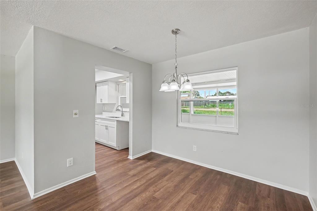 A dining area with wood-look flooring, a chandelier, and a view into a white kitchen — 3410 50TH STREET W, BRADENTON, FL