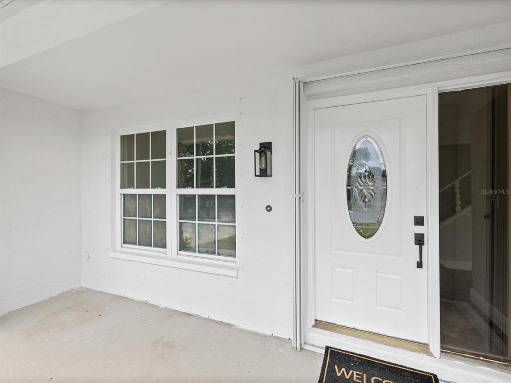 A white front door with an oval glass insert sits beside a window on a porch — 1972 LANSING DRIVE, CLEARWATER, FL