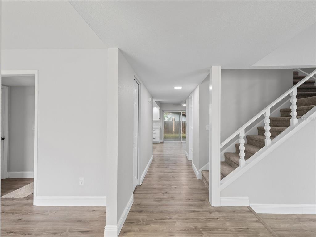 A hallway with light wood-look flooring leads to a sliding glass door near a staircase — 1972 LANSING DRIVE, CLEARWATER, FL