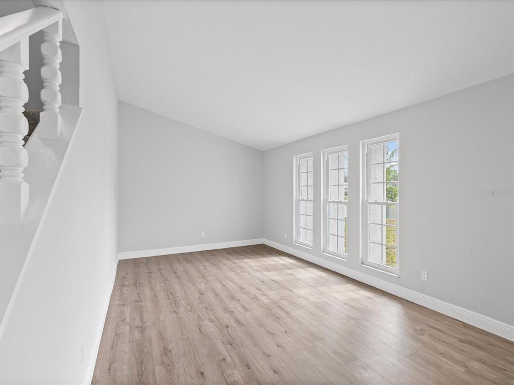 An empty room with light gray walls, wood-look flooring, and three tall windows — 1972 LANSING DRIVE, CLEARWATER, FL