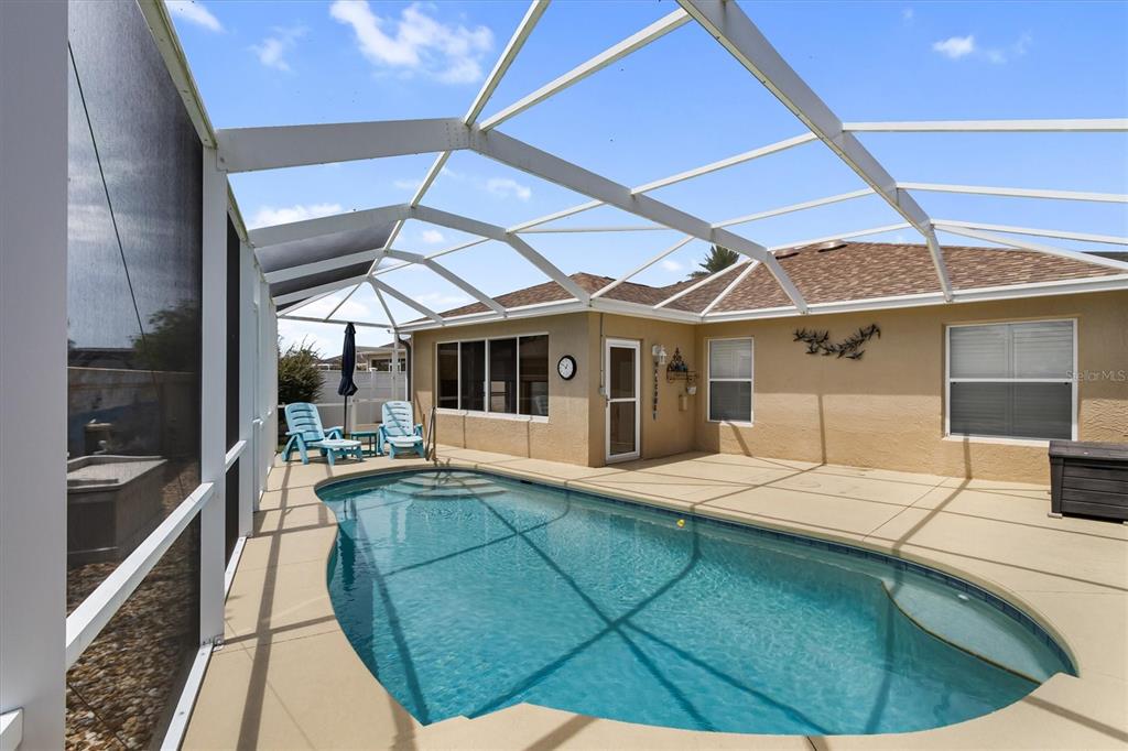 A swimming pool with a screened-in enclosure sits on a concrete patio behind a house — 1068 BURNETTOWN PLACE, THE VILLAGES, FL