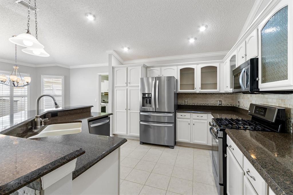 A kitchen features white cabinets, dark granite countertops, stainless steel appliances, and tile flooring — 1068 BURNETTOWN PLACE, THE VILLAGES, FL