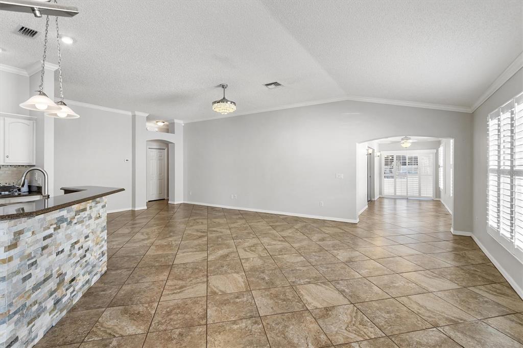 An open-concept living area features tile flooring, a stone-faced kitchen island, and arched entryways — 1068 BURNETTOWN PLACE, THE VILLAGES, FL