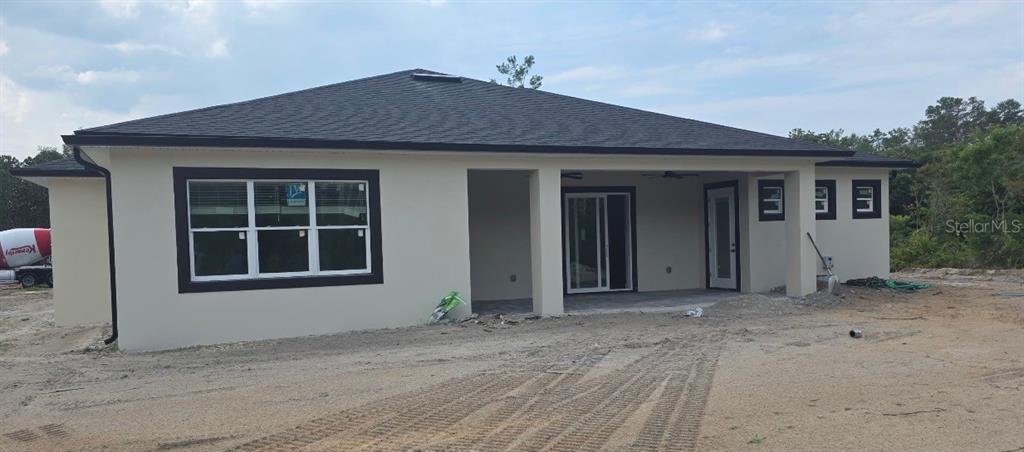 The exterior of a single-story house features light-colored stucco walls, dark trim, and a covered patio — 30643 APRICOT AVENUE, EUSTIS, FL