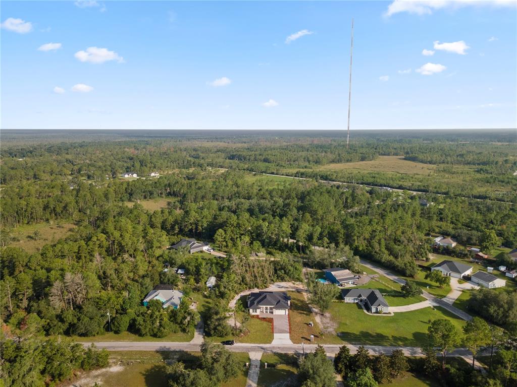An aerial view shows a modern house with a dark roof surrounded by wooded lots — 30643 APRICOT AVENUE, EUSTIS, FL