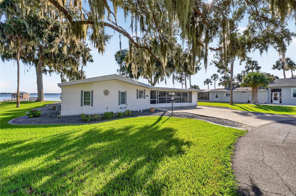 A white mobile home with a screened porch sits on a grassy lot near water — 38310 LANGLOIS PLACE, LEESBURG, FL