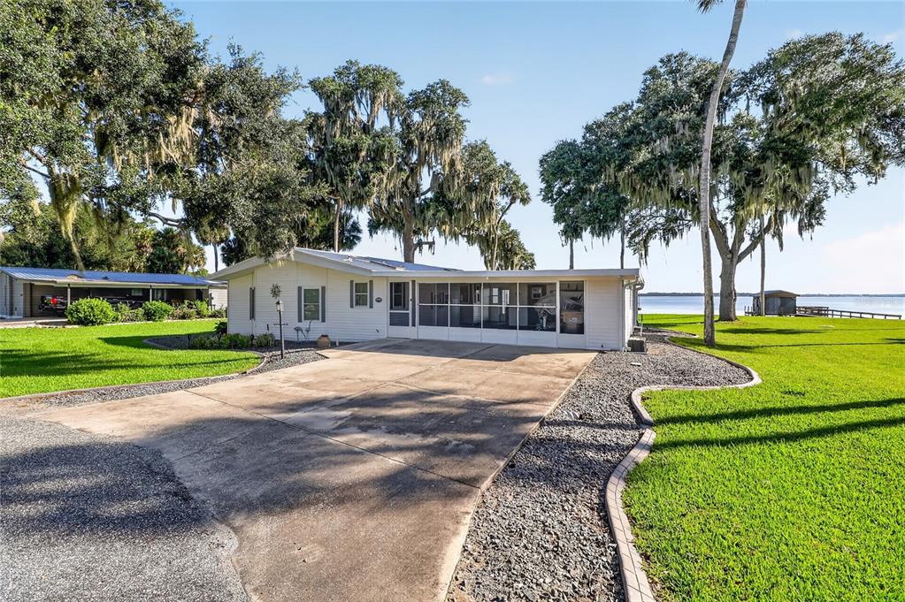 A single-story mobile home with a screened porch sits on a grassy lot near water — 38310 LANGLOIS PLACE, LEESBURG, FL