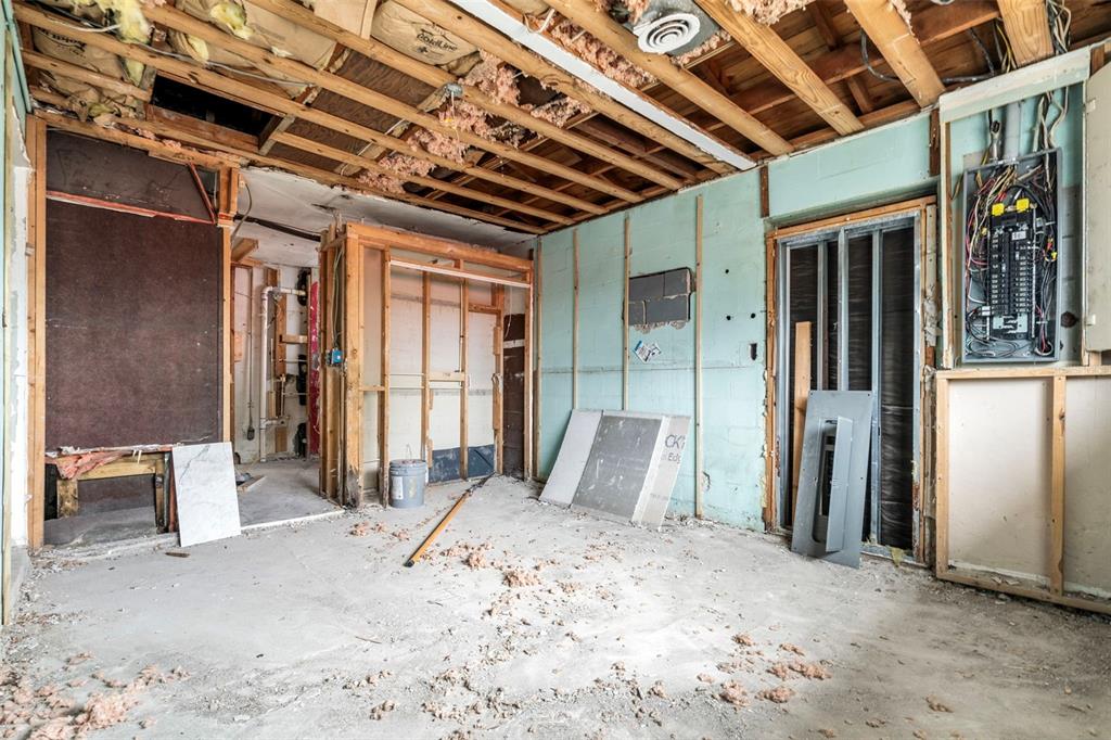 An unfinished room under renovation with exposed ceiling joists, wall studs, and an open electrical panel — 9570 SUN ISLE DRIVE NE, ST PETERSBURG, FL