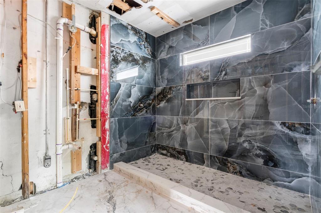 A bathroom under construction features a tiled shower stall with dark marble-patterned walls — 9570 SUN ISLE DRIVE NE, ST PETERSBURG, FL