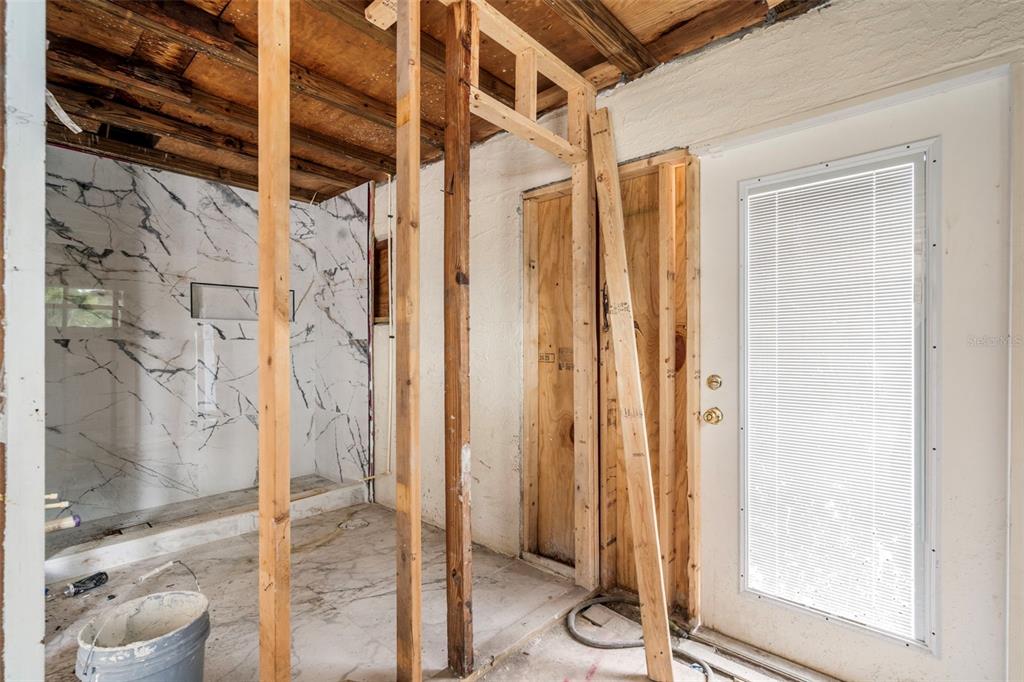 An unfinished bathroom renovation features exposed wood framing, marble-look wall tiles, and a glass door — 9570 SUN ISLE DRIVE NE, ST PETERSBURG, FL