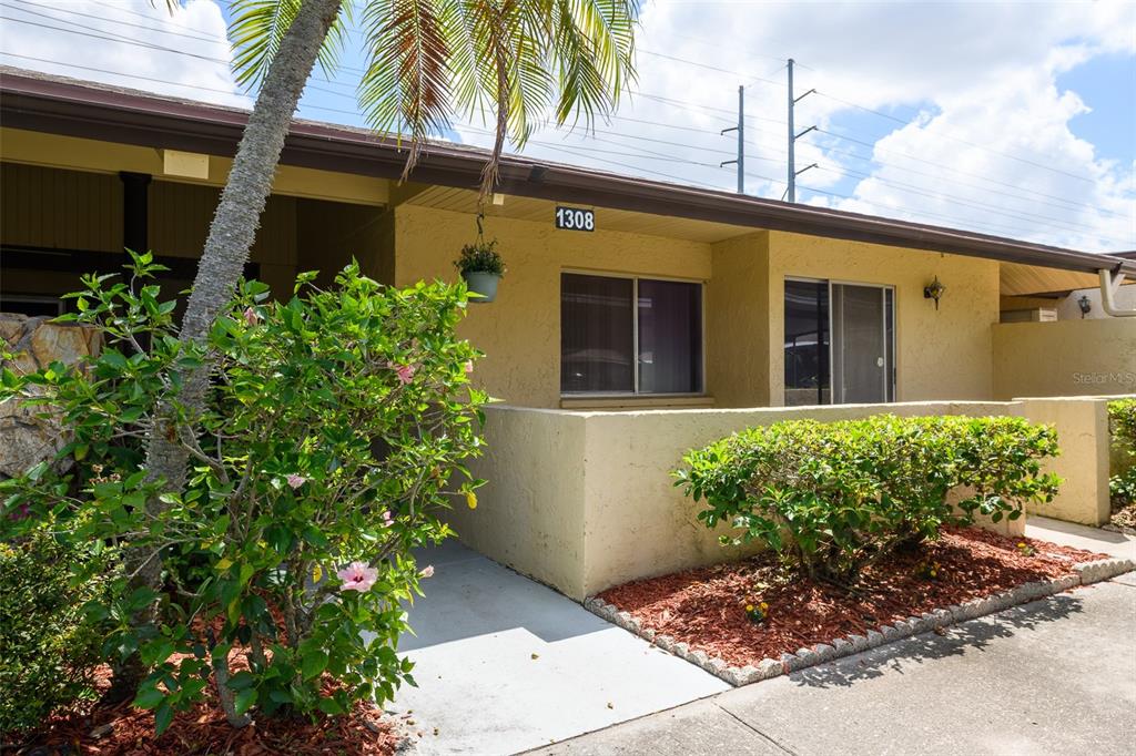 The exterior of a single-story tan building features a small patio, landscaping, and palm trees — 1308 13TH CIRCLE SE, LARGO, FL