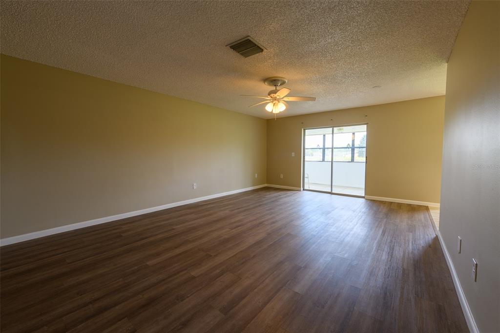 An empty living room features wood-look flooring, tan walls, a ceiling fan, and sliding glass doors — 1308 13TH CIRCLE SE, LARGO, FL