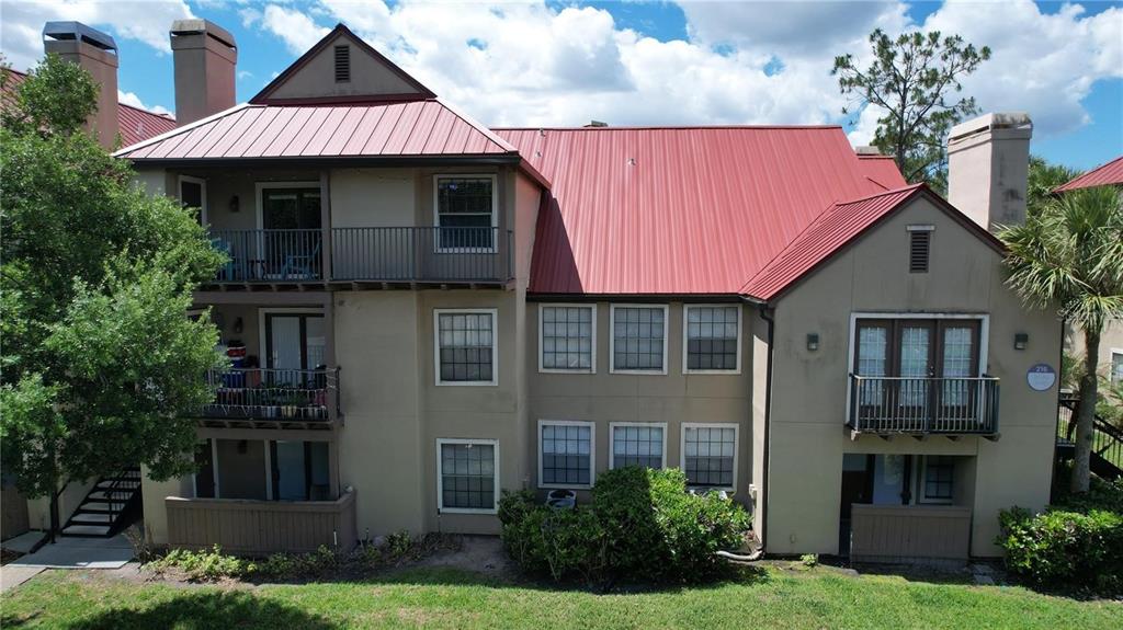 A multi-story apartment building features a red metal roof, tan stucco walls, and balconies — 232 AFTON SQUARE UNIT 207, ALTAMONTE SPRINGS, FL