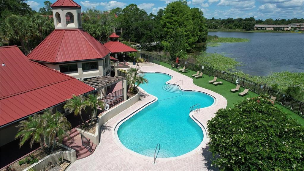 An aerial view shows a community swimming pool with a red-roofed clubhouse beside a lake — 232 AFTON SQUARE UNIT 207, ALTAMONTE SPRINGS, FL