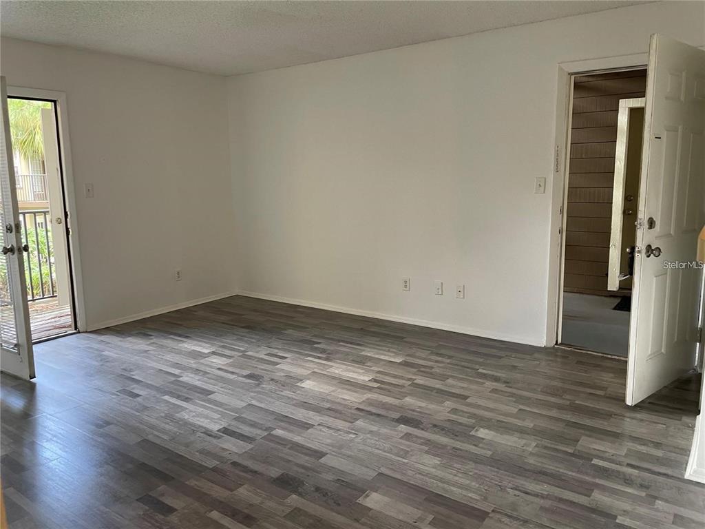 An empty room features gray wood-look flooring, white walls, a glass balcony door, and an entryway — 232 AFTON SQUARE UNIT 207, ALTAMONTE SPRINGS, FL