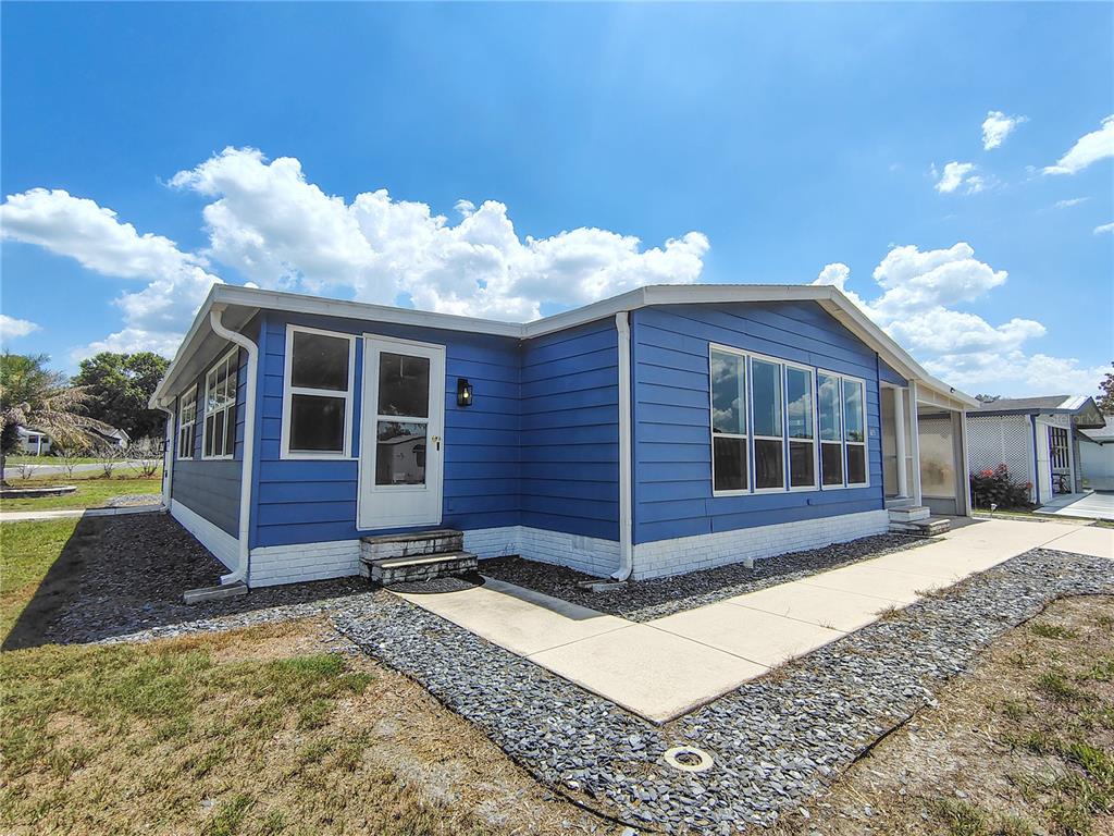 A blue mobile home with white trim and a concrete walkway sits on a gravel lot — 702 TURNBERRY LANE, LADY LAKE, FL