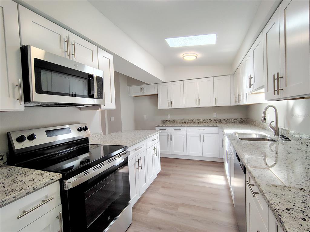 A kitchen features white cabinets, granite countertops, stainless steel appliances, and light wood-look flooring — 702 TURNBERRY LANE, LADY LAKE, FL