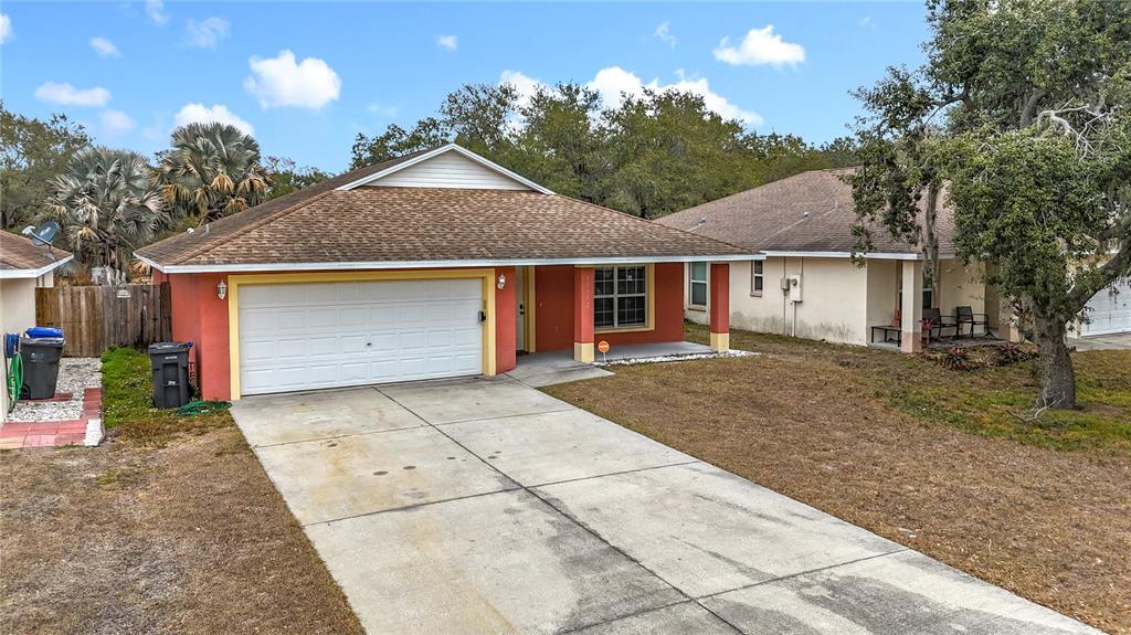 A single-story house with a red exterior, a two-car garage, and a concrete driveway — 11112 HIDDEN BREEZE DRIVE, WIMAUMA, FL