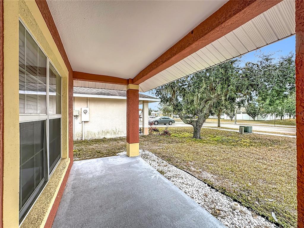 A covered concrete porch overlooks a grassy yard with a large tree and a street — 11112 HIDDEN BREEZE DRIVE, WIMAUMA, FL