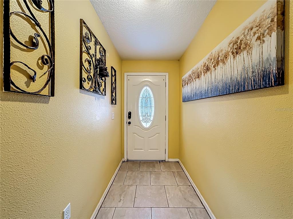 An entryway features yellow walls, tile flooring, a white front door, and decorative wall art — 11112 HIDDEN BREEZE DRIVE, WIMAUMA, FL