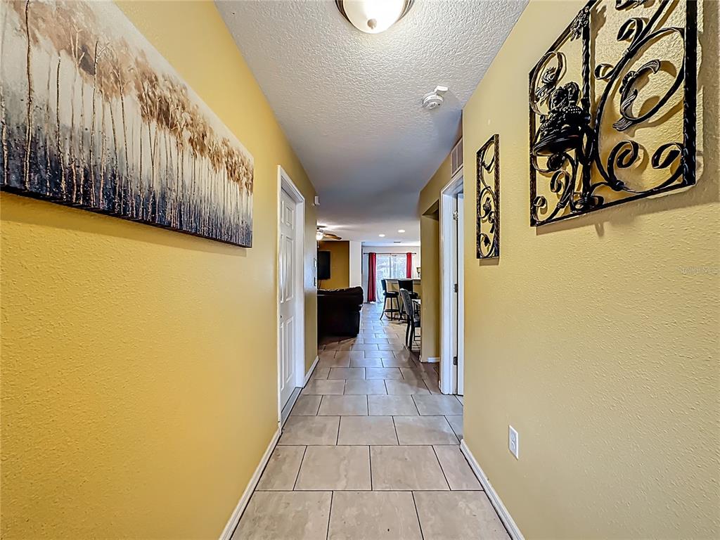 A hallway with yellow walls, tile flooring, and wall art leads toward an open living area — 11112 HIDDEN BREEZE DRIVE, WIMAUMA, FL