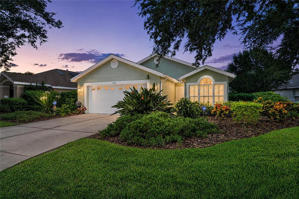 A single-story house with a white garage, arched window, and landscaped front yard at dusk — 7488 ELEANOR CIRCLE, SARASOTA, FL