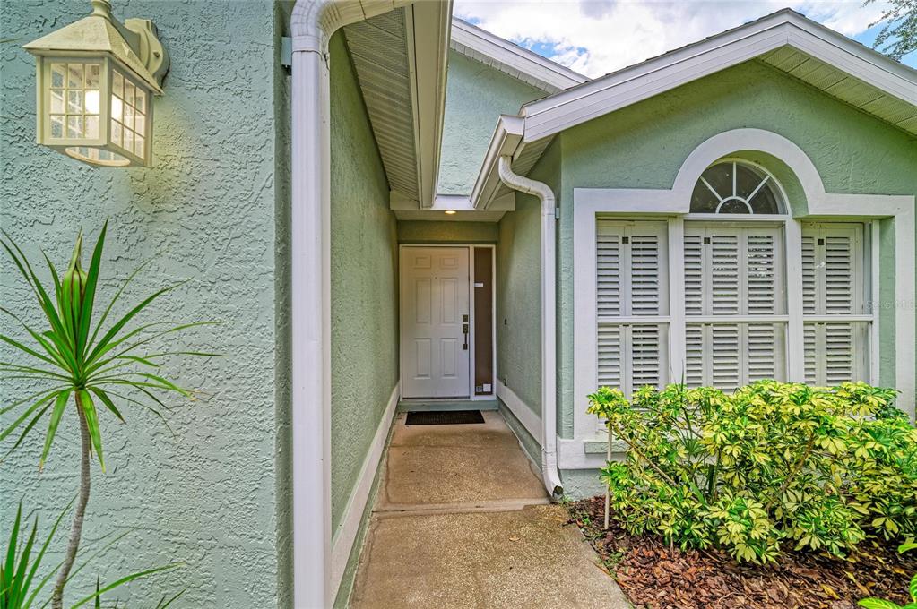 A light green house exterior features a white front door, arched window, and outdoor lighting — 7488 ELEANOR CIRCLE, SARASOTA, FL