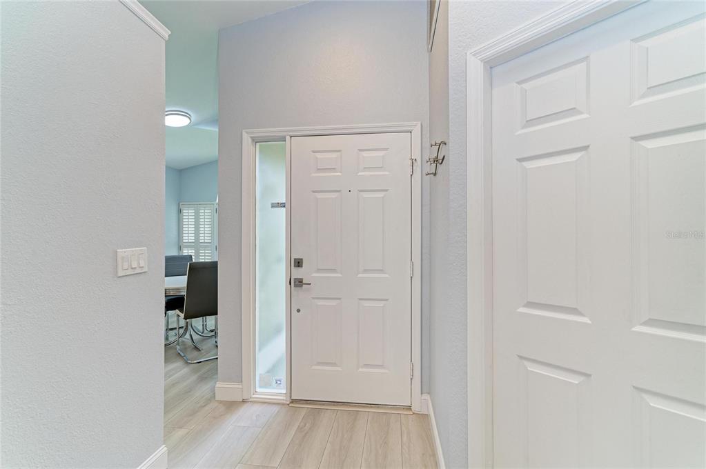 An entryway features a white front door with a sidelight, light wood flooring, and walls — 7488 ELEANOR CIRCLE, SARASOTA, FL