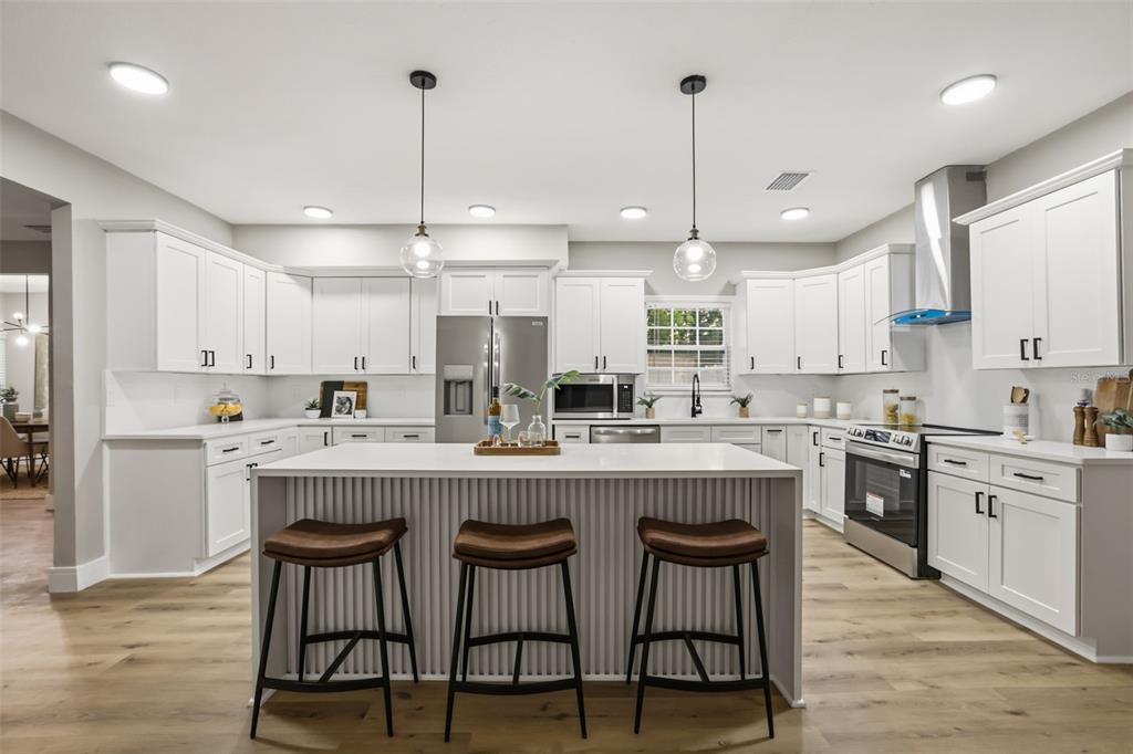 A modern white kitchen features a central island with three stools and wood-look flooring — 15 E LAUREL STREET, APOPKA, FL