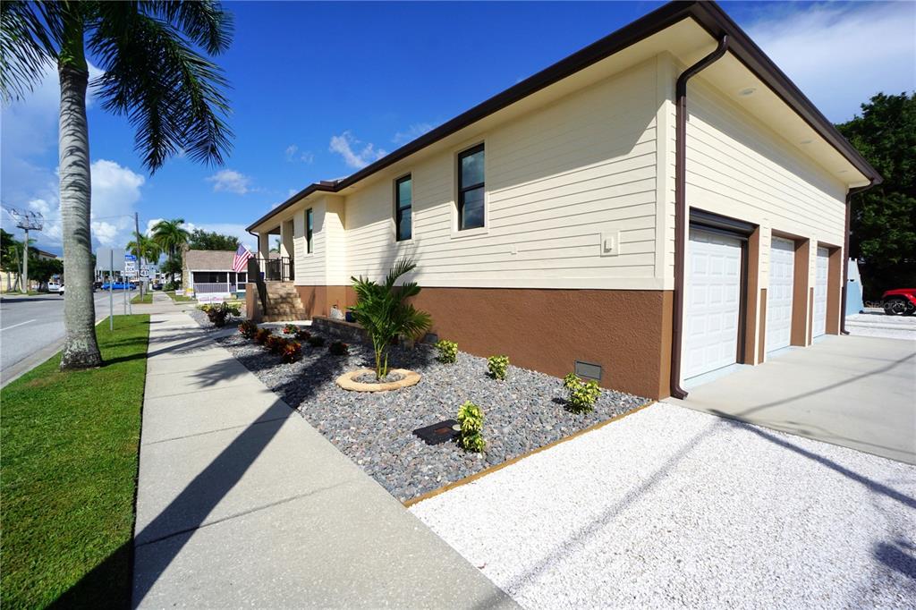 A beige house with a brown base and three garage doors sits beside a sidewalk — 301 GOLDSTEIN STREET, PUNTA GORDA, FL