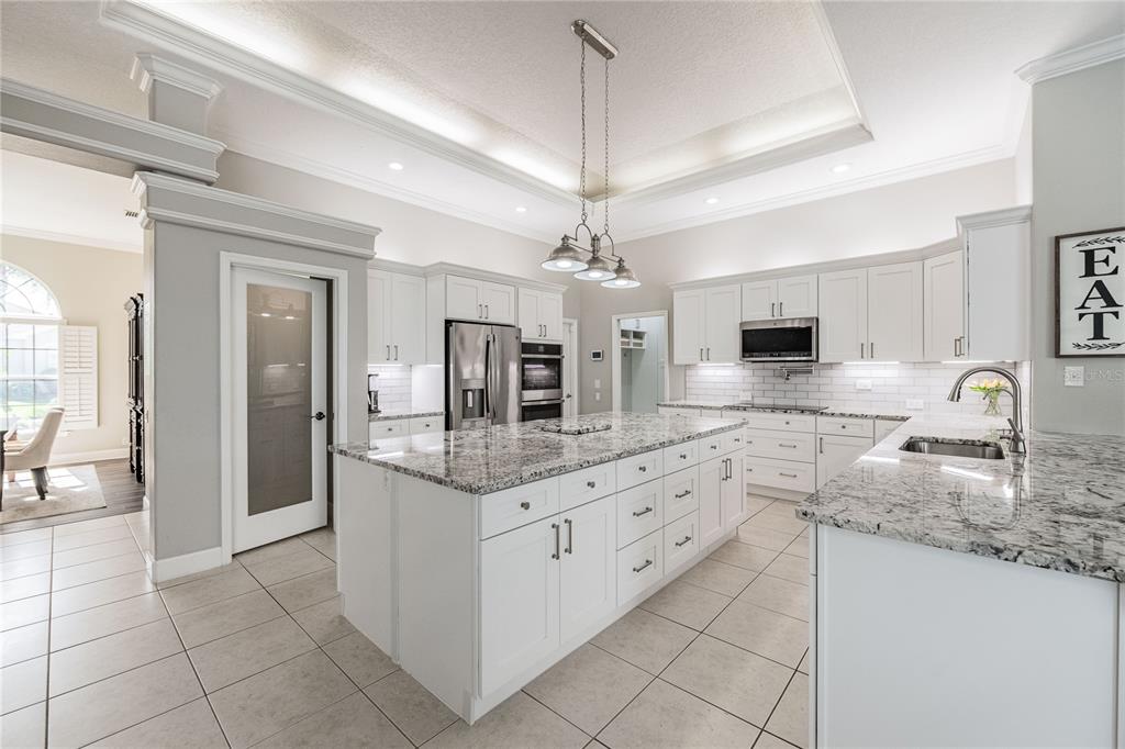 A modern white kitchen features a large granite-topped island, stainless steel appliances, and tile flooring — 1221 VISTA HILLS DRIVE, LAKELAND, FL