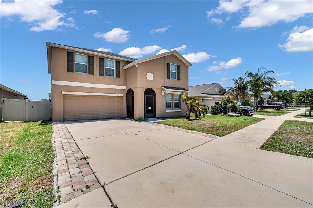 A two-story beige house with a two-car garage and a concrete driveway under blue skies — 1739 BROAD WINGED HAWK DRIVE, RUSKIN, FL