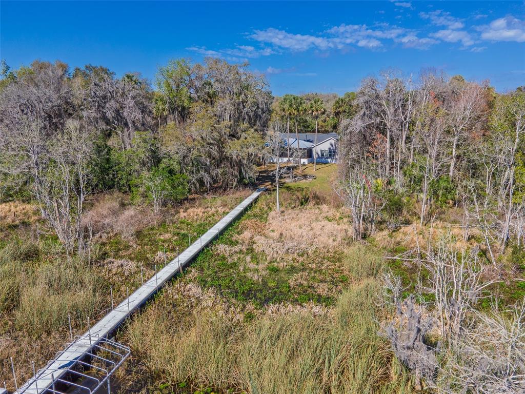 An aerial view shows a long wooden dock extending through marshland toward a house — 17482 SE 34TH LANE, OCKLAWAHA, FL