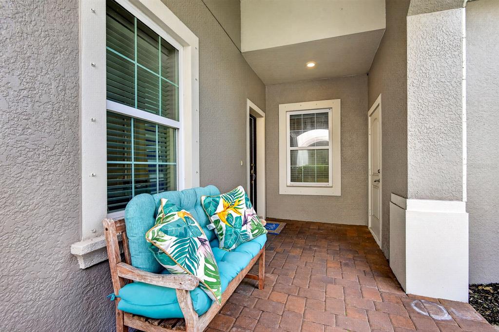 A covered porch features a wooden bench with teal cushions, a brick floor, and two windows — 7108 PLAYA BELLA DRIVE, BRADENTON, FL