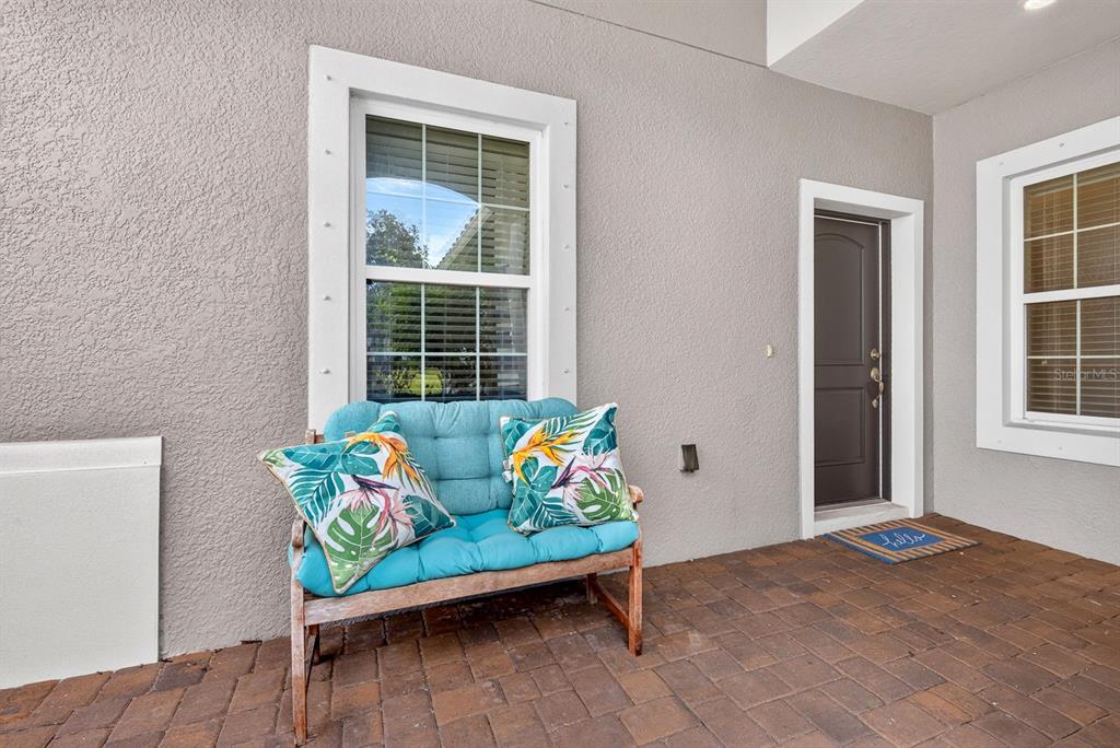 A covered patio features a wooden bench with blue cushions, a dark door, and windows — 7108 PLAYA BELLA DRIVE, BRADENTON, FL