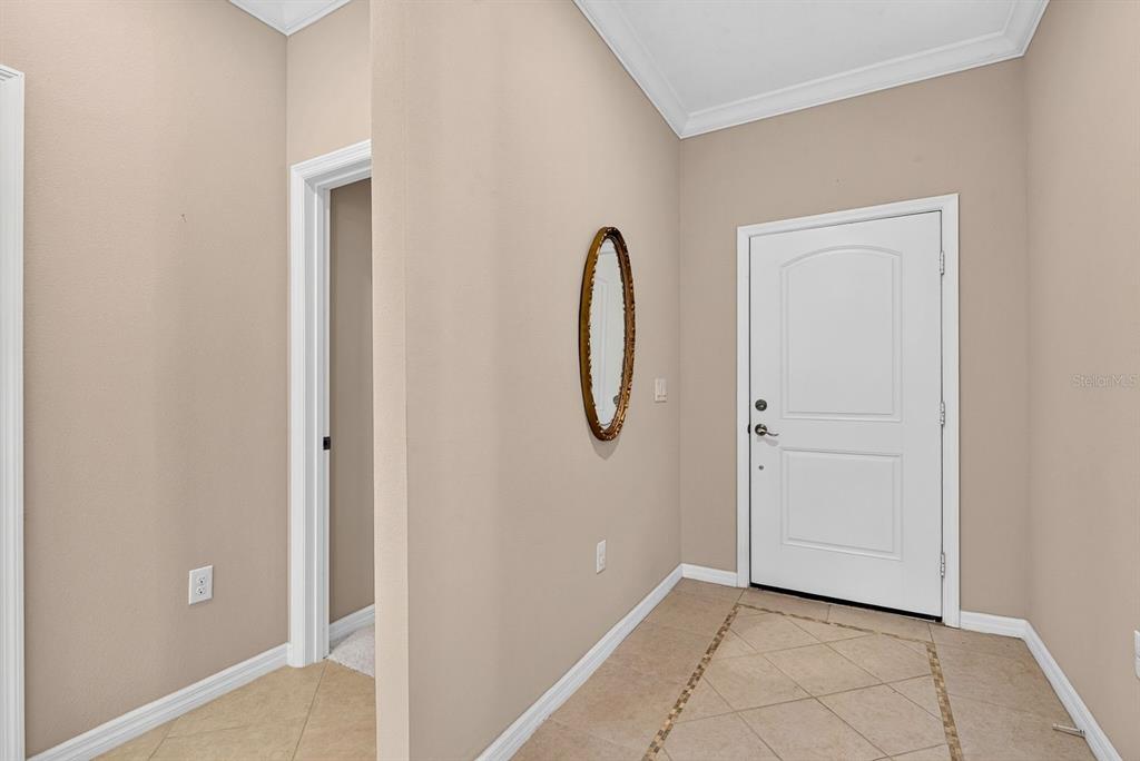 An entryway features beige walls, tiled flooring, a white door, and an oval wall mirror — 7108 PLAYA BELLA DRIVE, BRADENTON, FL