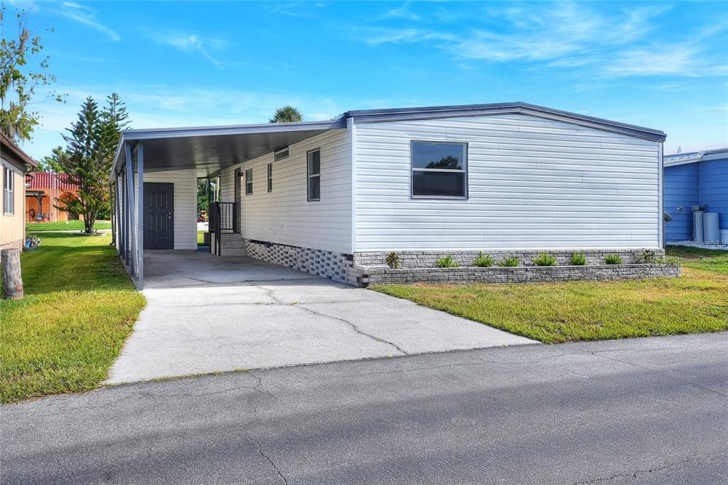 A single-story manufactured home features a large carport, white siding, and a landscaped front yard — 2055 S FLORAL AVENUE UNIT 55, BARTOW, FL