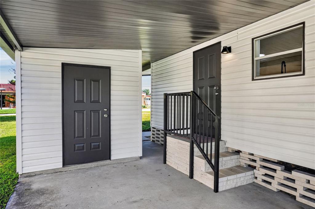 A covered concrete patio features two dark doors, a small staircase, and white siding — 2055 S FLORAL AVENUE UNIT 55, BARTOW, FL