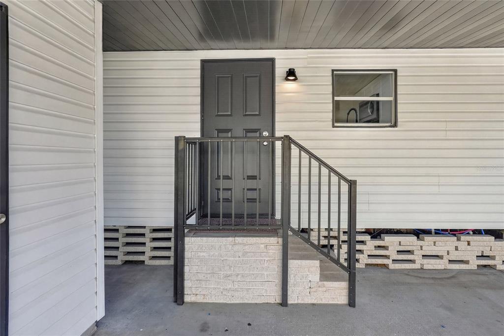 A dark gray door with a metal railing sits atop a brick-faced porch entrance — 2055 S FLORAL AVENUE UNIT 55, BARTOW, FL