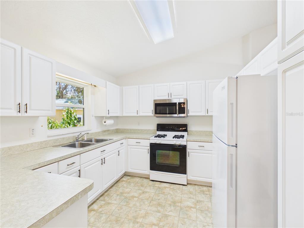 A kitchen features white cabinets, laminate countertops, a white refrigerator, and a stainless steel microwave — 11236 N RAIN POINT, INGLIS, FL