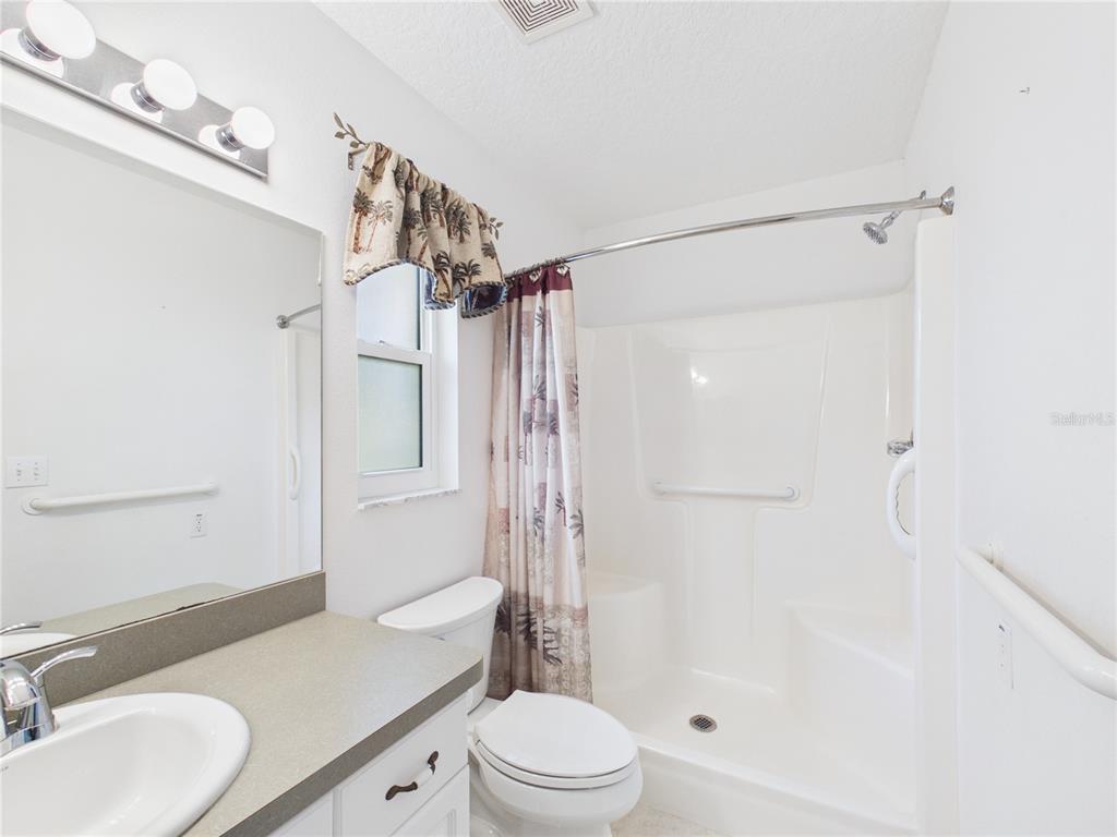 A bathroom features a white vanity, a toilet, and a shower stall with a curtain — 11236 N RAIN POINT, INGLIS, FL