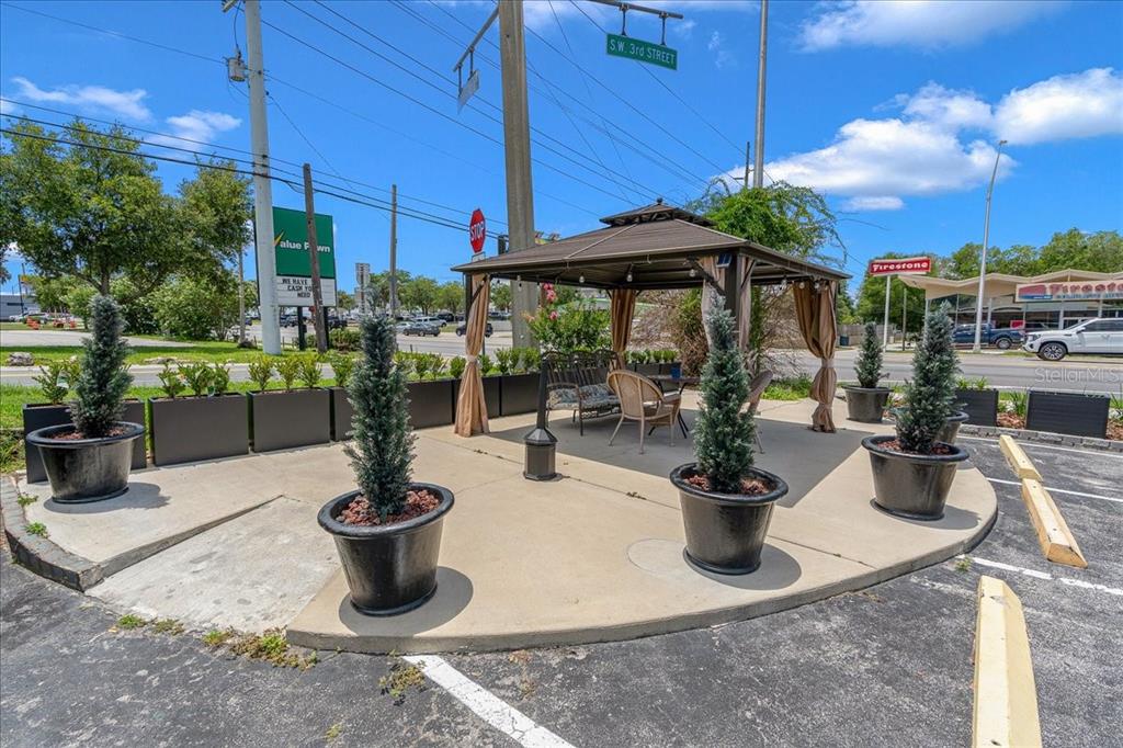 A gazebo with outdoor seating sits on a concrete patio surrounded by potted evergreen trees — 215 S PINE AVENUE, OCALA, FL