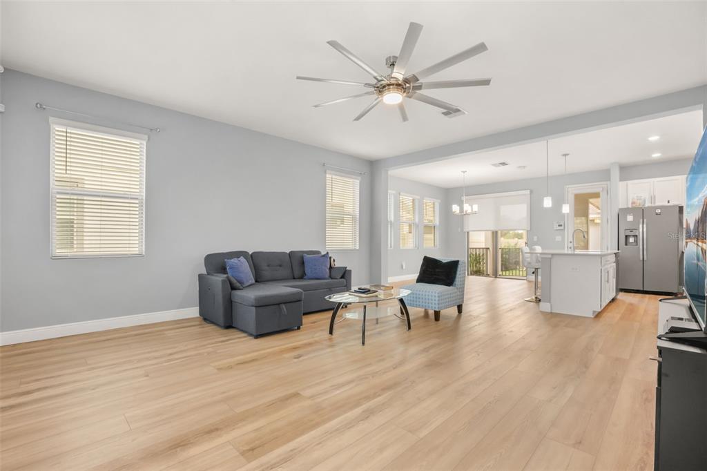 A living room with light wood floors, a grey sectional sofa, and an open kitchen — 154 WOODED VINE DRIVE, WINTER SPRINGS, FL