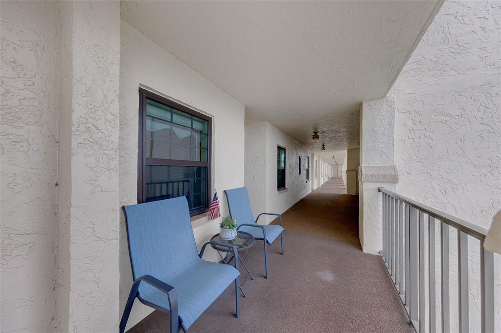 A covered outdoor balcony features two blue chairs, a small table, and a metal railing — 19029 US HIGHWAY 19 N UNIT 26-204, CLEARWATER, FL