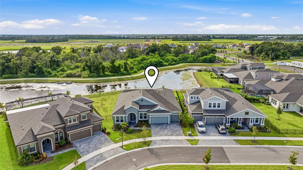 An aerial view shows three suburban houses with paved driveways situated along a pond — 5254 WOLF CREEK DRIVE, APOLLO BEACH, FL
