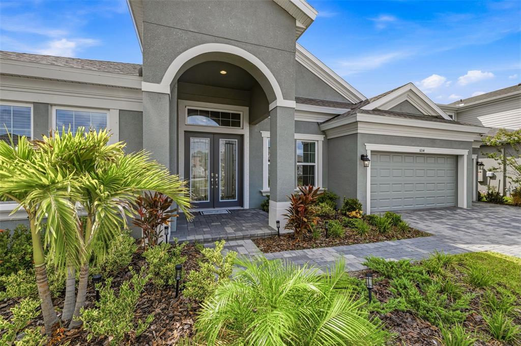 A gray stucco house features a covered arched entryway, double front doors, and a garage — 5254 WOLF CREEK DRIVE, APOLLO BEACH, FL