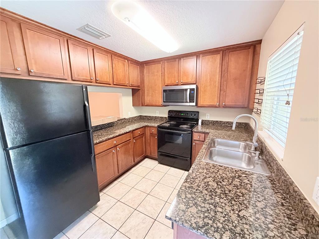 A kitchen features wood cabinets, dark granite countertops, a black stove, and a double sink — 110 COQUINA BAY DRIVE, ST PETERSBURG, FL